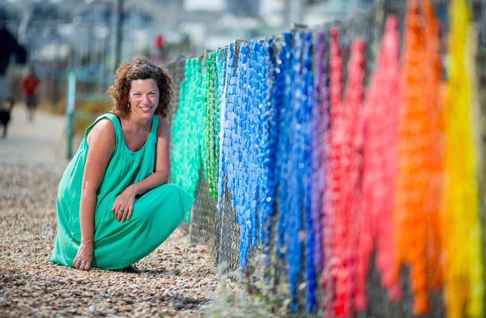 Woman crouching down smiling at camera next to colourful fence