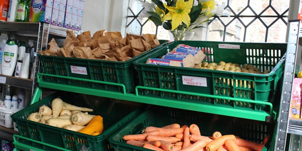 Four green vegetable baskets in a community food hub that contain fresh carrots, parsnips, potatoes and eggs, with labels saying 'free veggies'.