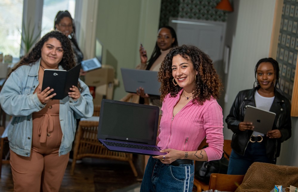 Group of woman holding a mix of laptops and tablets smiling at the camera