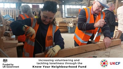 Photo of two ASAN Wood Saints volunteers taking apart wooden pallets side by side.  