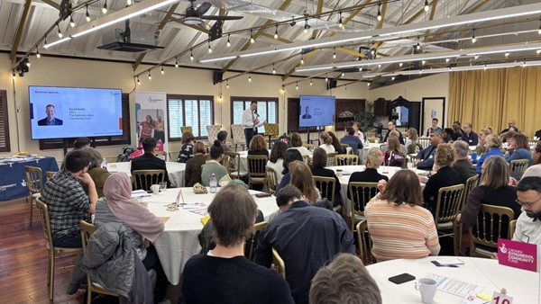 Indoor conference setting with Davitt Knott, CEO at NLCF, speaking into a microphone at the front of a seated audience 