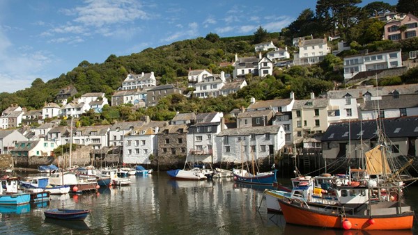 Small harbourside town in Cornwall, with old houses next to some working boats, set under blue skies.