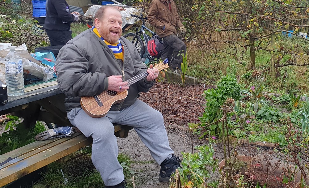 Man siting on bench playing a small guitar