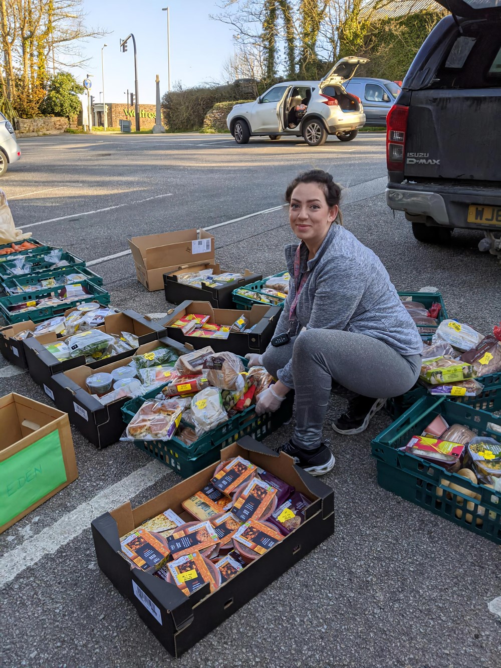 Lady crouching down surrounded by food trays in car park