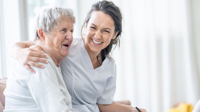 photo of a young woman in an NHS uniform sat laughing with an older woman